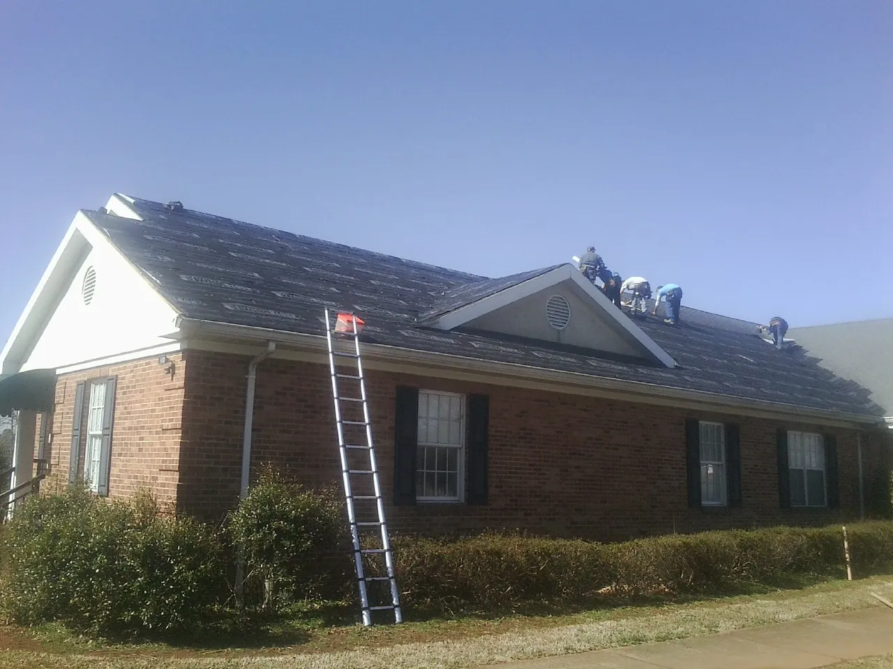 Crew tearing shingles off a brick ranch roof with a ladder set — Emergency Roof Repair work by our crew in Ramsay