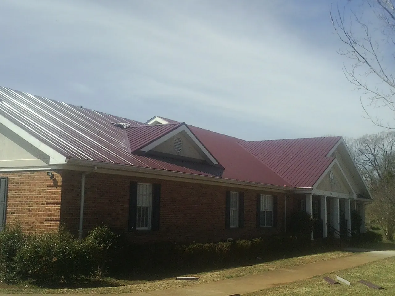 Red metal roof with gabled entries on a long brick building, from a Hail Damage Roof Repair job in Ramsay