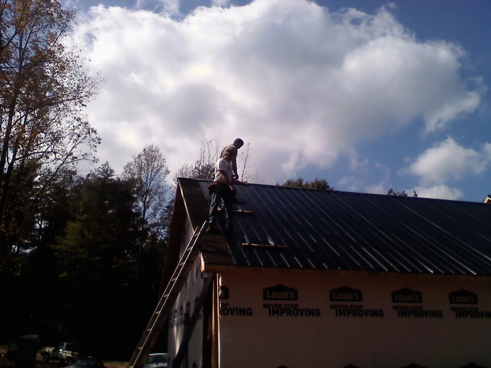 Roofer fastening dark metal panels high against a cloudy sky, from a Roof Inspection job in Ramsay