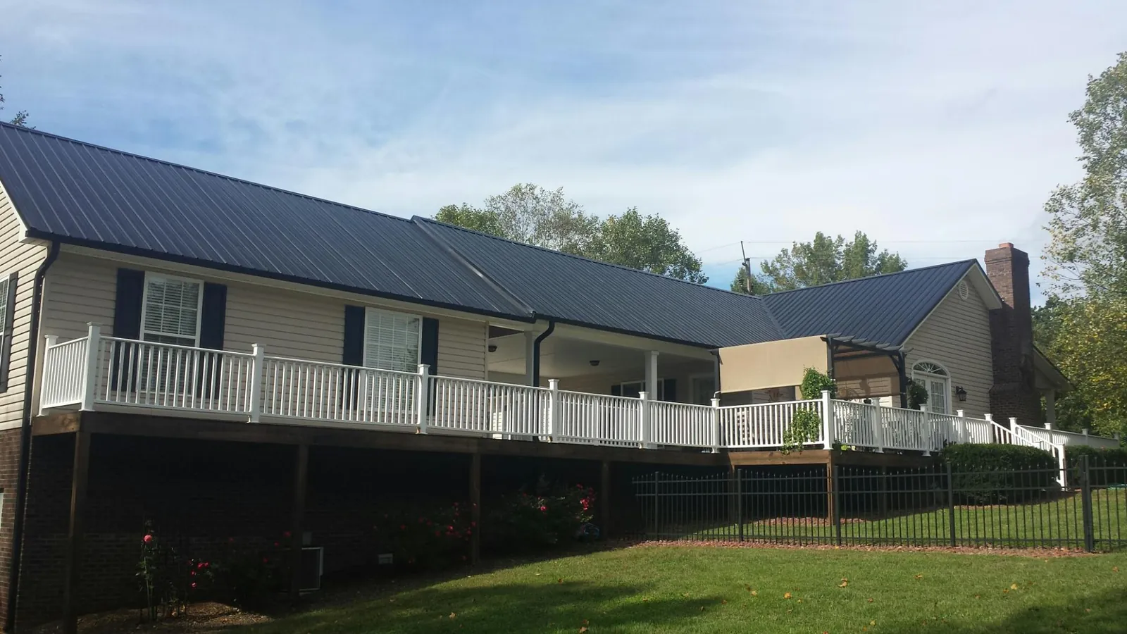 Black metal roof above a long white railed deck on a hillside home in Ramsay