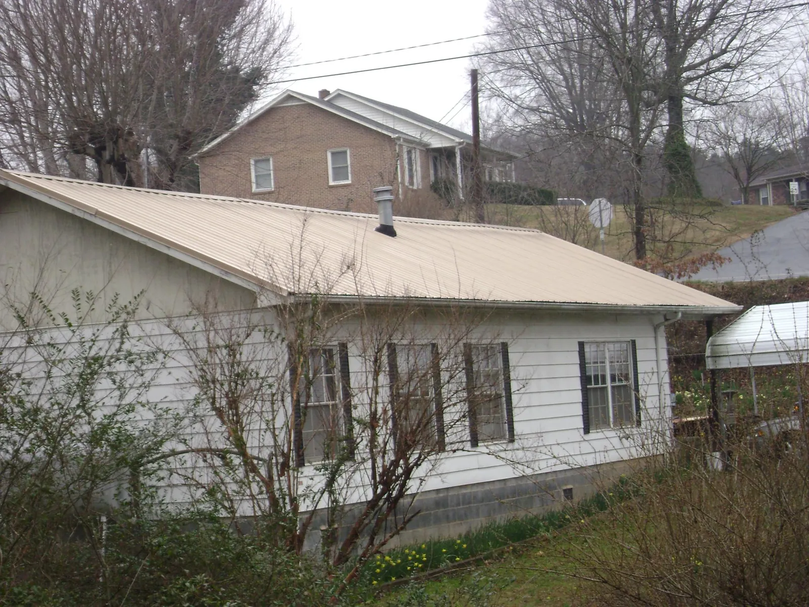 Tan metal roof on a white sided house set into a hillside — Commercial Roofing by Roofing Brothers in Ramsay